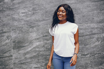 Cute black girl near gray wall. Lady in a white t-shirt and blue jeans.