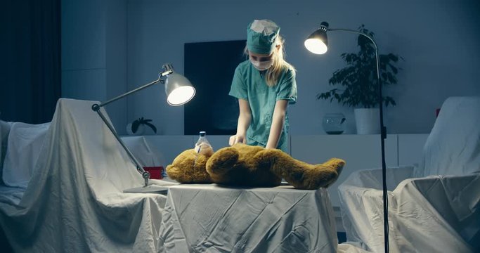 Cute little girl wearing doctor suit playing at home, pretending to be a surgeon, providing medical care to her teddy bear. Shot on RED Cinema camera with Cooke Prime lenses