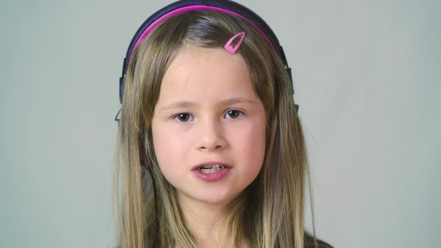 Pretty smiling cild girl listening to music in big pink earphones.