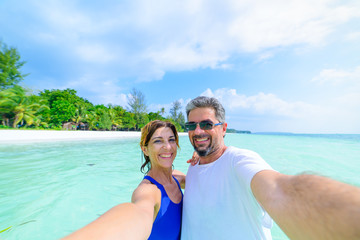 Happy man and woman taking selfie in tropical caribbean sea. Adult mid age traveling couple, real people having fun in vacation.