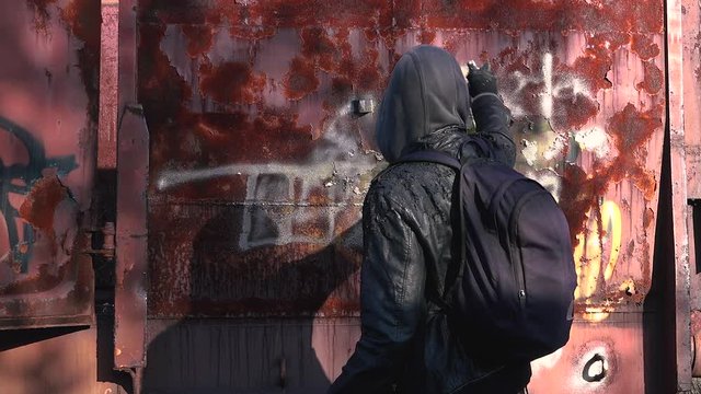 Homeless man paint spraying abandoned train wagon with aerosol can