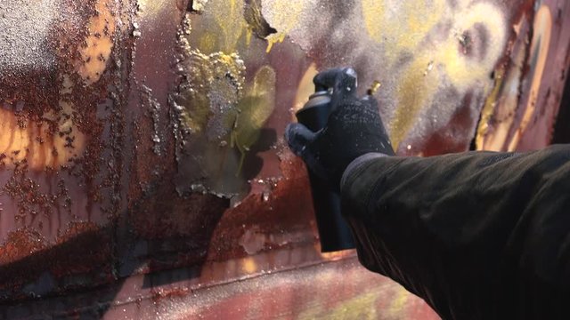Homeless man paint spraying abandoned train wagon with aerosol can