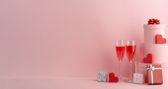 Glasses of red sparkling wine, gift boxes and red hearts on pink background