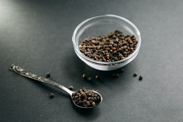 Spices on black background. Black pepper in a bowl.
