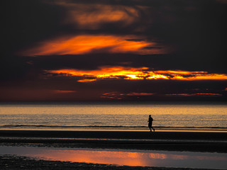 Fototapeta premium Single person running at an empty beach after colorful sunset in northern France