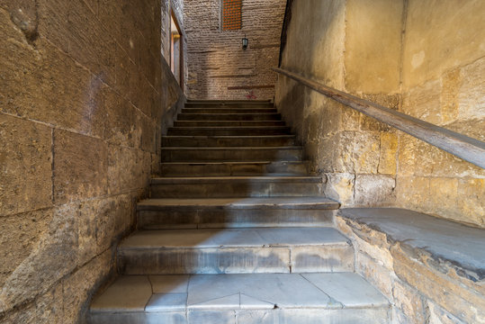 Old narrow stone staircase leading to stone bricks wall with closed window