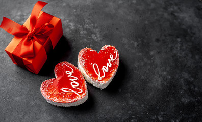 Obraz na płótnie Canvas Two Cheesecake - a heart-shaped cake with the inscription love and a gift with a red ribbon for Valentines Day on a stone background with copy space for your text