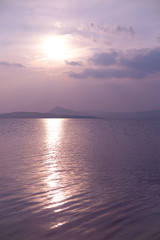 Ripples on the lake. Violet sunset. Solar path and the sun. The concept of relaxation and calm.