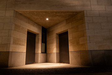 Two doors and a lamp in a triangular niche, two doors and sandstone facade at night, modern architecture