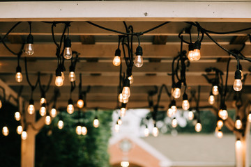 Hanging vintage string lights w on a wooden pergola beams patio in a backyardith edison bulbs  - obrazy, fototapety, plakaty