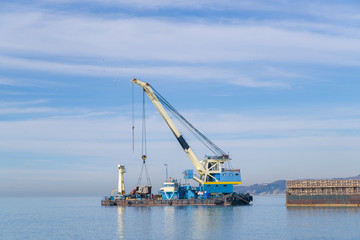 Fototapeta premium floating crane on a barge near the shore. Construction work in the sea. Construction of engineering structures on the water 