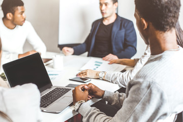 A team of young office workers, businessmen with laptop working at the table, communicating together in an office. Corporate businessteam and manager in a meeting. coworking.