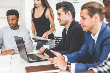A team of young office workers, businessmen with laptop working at the table, communicating together in an office. Corporate businessteam and manager in a meeting. coworking.