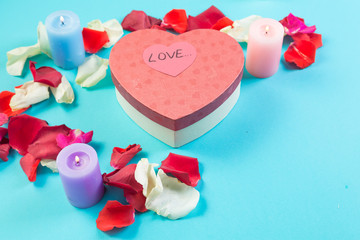 Heart of rose petals on a blue background and a heart-shaped box with a gift and signature Love.