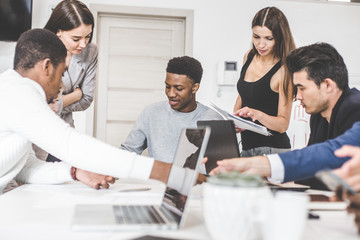 A team of young office workers, businessmen with laptop working at the table, communicating together in an office. Corporate businessteam and manager in a meeting. coworking.
