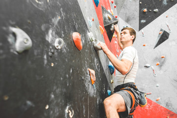 Sportsman climber moving up on steep rock, climbing on artificial wall indoors. Extreme sports and...