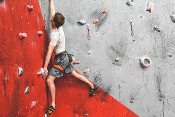 Sportsman climber moving up on steep rock, climbing on artificial wall indoors. Extreme sports and...