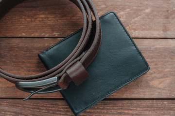 Dark brown men's belt and black wallet on wooden desk