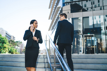 Elegant business people on street stairway Contemporary formal diverse woman speaking on mobile phone walking on stairs near businessman on urban background in back lit