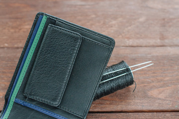 Close up Men's black leather wallet on wooden boards and threads, needles.