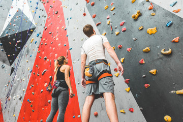 couple of athletes climber stand and watch on steep rock, climbing on artificial wall indoors. Extreme sports and bouldering concept. - obrazy, fototapety, plakaty