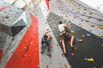 couple of athletes climber moving up on steep rock, climbing on artificial wall indoors. Extreme sports and bouldering concept - obrazy, fototapety, plakaty