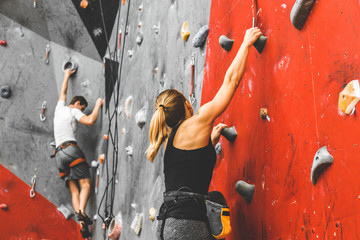 Sportswoman climber moving up on steep rock, climbing on artificial wall indoors. Extreme sports and bouldering concept - obrazy, fototapety, plakaty