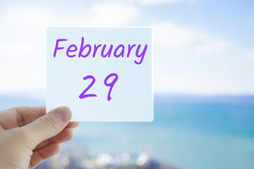 February 29th, last day of the winter. Hand holding sticker with text February 29 on the blurred background of the sea and sky. Copy space for text. Month in calendar concept