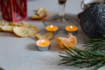 Fototapeta na wymiar Christmas candles and tangerines on the table against the background of New Year's decor. Christmas association.