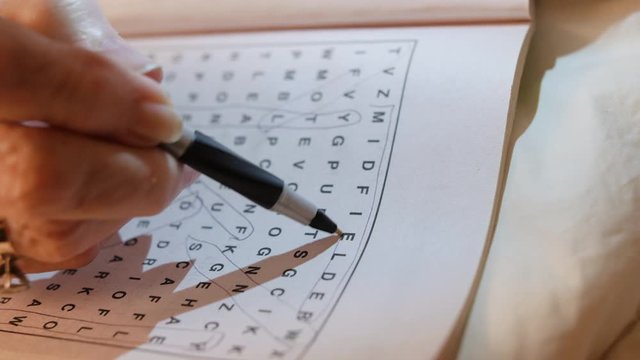 Closeup of female hand circling letters in word seek and find puzzle book.