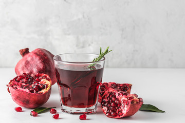 Glass of pomegranate juice with fresh pomegranate fruits and rosemary on marble table. Healthy drink