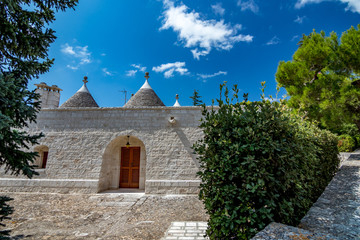 Fototapeta na wymiar Roofs and entrance of truli, typical whitewashed cylindrical houses in Alberobello, Puglia, Italy with amazing blue sky with clouds, street view