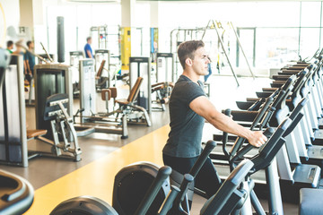 The athletic man dressed in a black sportswear running on the eleptic trainer in the modern gym