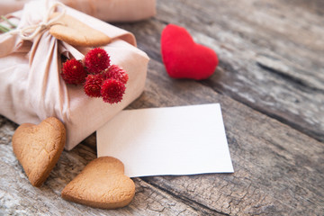 Stylish eco-friendly rustic gift wrapped in linen fabric with branch of red flowers on wooden background. Top view. Copy space. Flat lay. Simple eco presents plastic free.