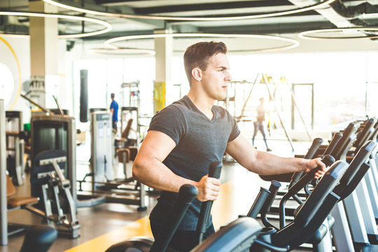 The athletic man dressed in a black sportswear running on the eleptic trainer in the modern gym