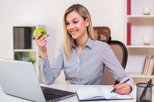 Businesswoman Eating Apple While Working In Her Office.	