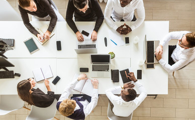 A team of young businessmen sitting at the table, top view, working and communicating together in an office. Corporate businessteam and manager in a meeting.