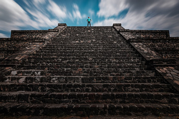 A traveler standing on the top of the Teotihuacan piramid. Time-lapse sky shows the concept of...