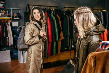 Beautiful brunette trendy woman with backpack trying warm rainy coat on clothes shop. shopping,
