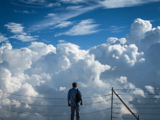 man stands on top of a mountain near abyss on a background of blue sky and white clouds on a sunny day