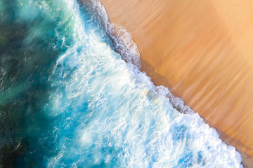 View from above, stunning aerial view of some waves crashing onto a beautiful beach during sunset....