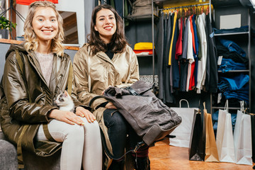 Two female friends in warm winter raincoat relaxing, choosing new clothes for their wardrobe