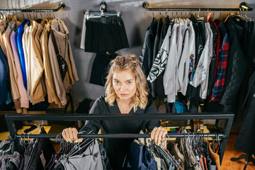 Cute blond girl has chosen a new lovely dress among a lot of clothes in modern store she is happy. Sale, gifts, holidays, beauty concept.