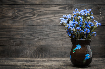 A vase with blue flowers stands on a wooden table. Wood texture.