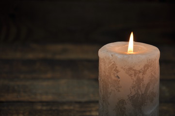 A large candle burns in the dark. On a wooden background.