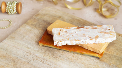 Three type of  Spanish turron, hard almond, soft almond and burnt egg yolk nougat on wooden cut board with Christmas decoration