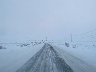 Empty road covering by white snow and some dry grass at side way with cloudy climate in winter season.