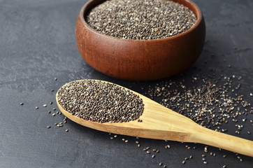Raw organic chia seeds superfood in wooden bowl and spoon on dark stony background.