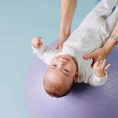 Obraz na płótnie Canvas baby boy in white overalls lies on a lilac fitness ball