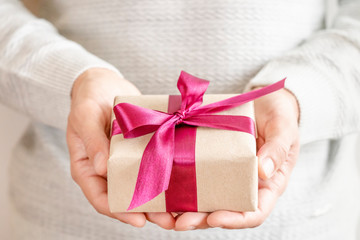 Man hands holding gift box over white sweater. Christmas, birthday, mother's day, Valentine's day concept.